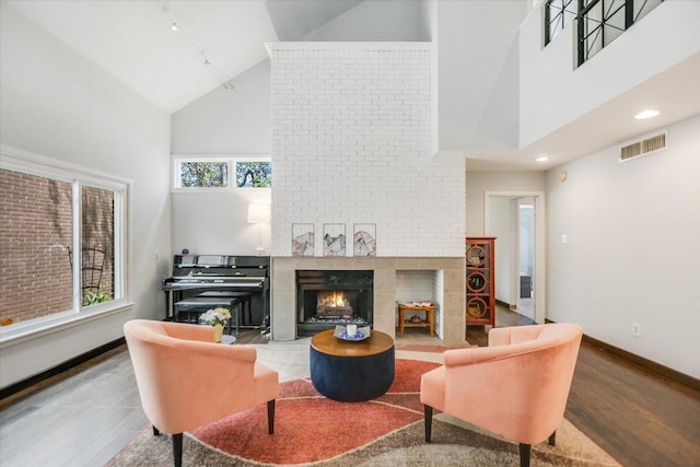 living area featuring visible vents, baseboards, wood finished floors, a large fireplace, and high vaulted ceiling