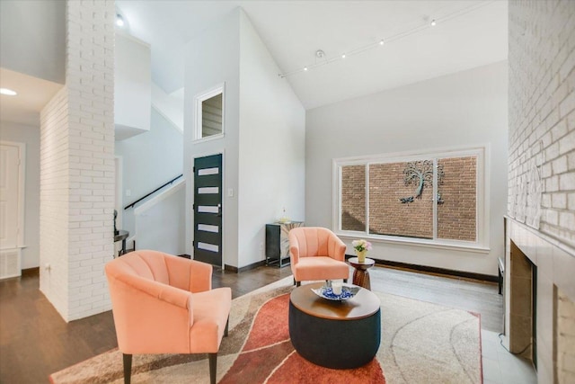 sitting room with high vaulted ceiling, wood finished floors, stairs, track lighting, and a fireplace