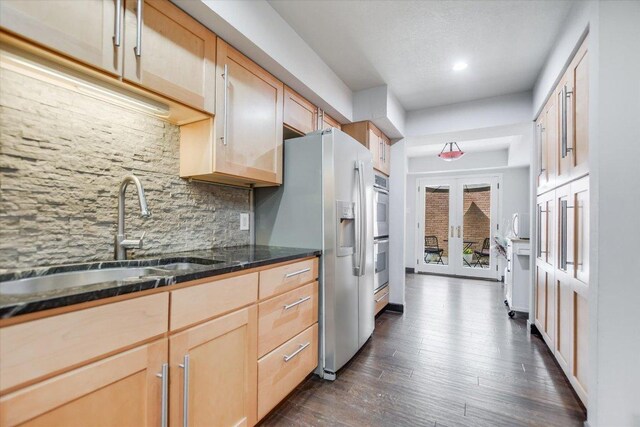 kitchen featuring dark wood finished floors, light brown cabinets, a sink, decorative backsplash, and appliances with stainless steel finishes