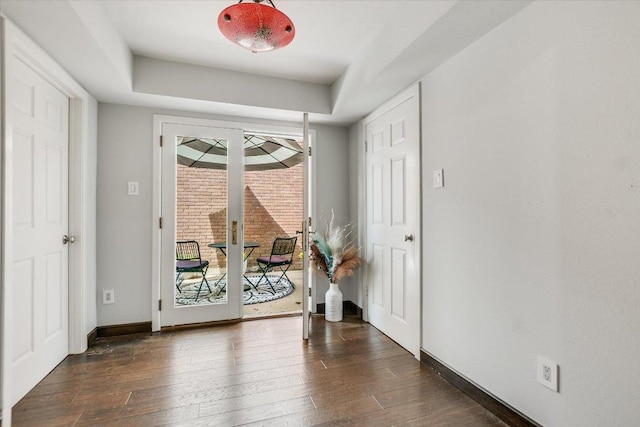 doorway to outside with baseboards, dark wood-type flooring, and a raised ceiling