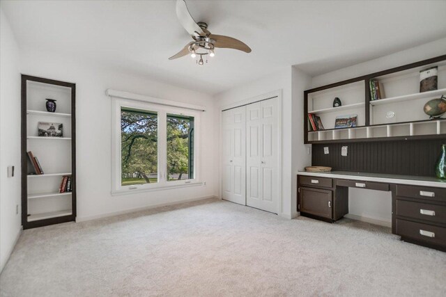 unfurnished office featuring baseboards, a ceiling fan, built in study area, and light colored carpet