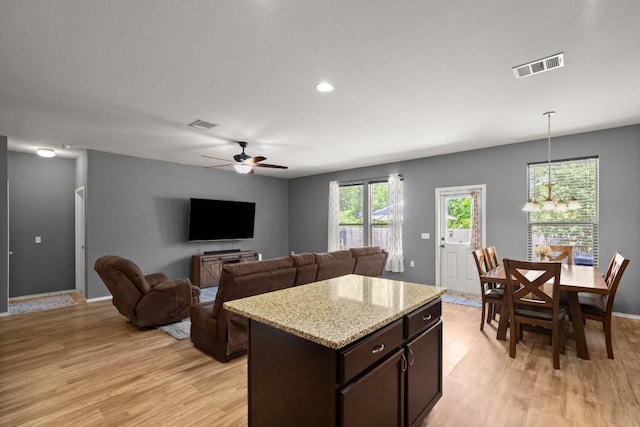 kitchen with light wood finished floors, dark brown cabinets, visible vents, ceiling fan with notable chandelier, and pendant lighting