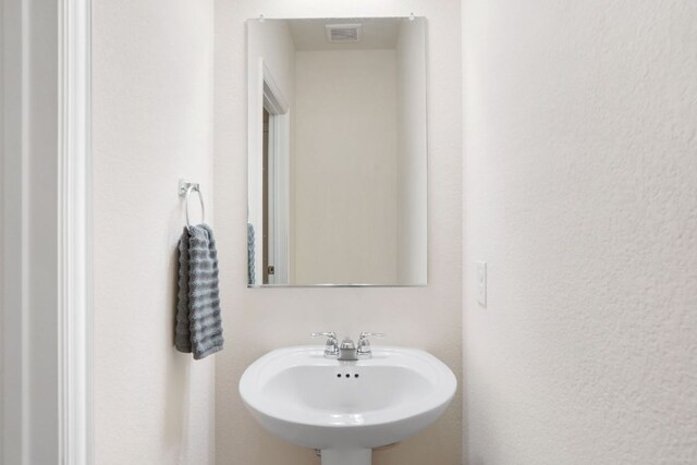 bathroom featuring a textured wall, a sink, and visible vents