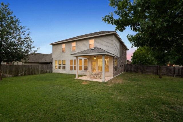 back of house at dusk with a fenced backyard, a patio area, a lawn, a shingled roof, and ceiling fan