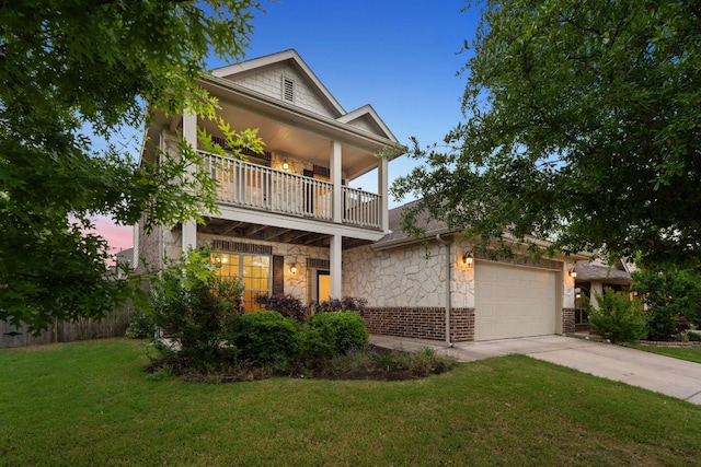 greek revival inspired property with a balcony, concrete driveway, stone siding, an attached garage, and a front yard