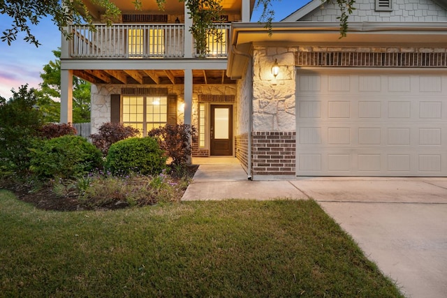 view of front of home with concrete driveway, stone siding, a balcony, and a lawn