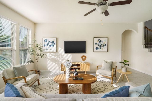 tiled living area featuring a ceiling fan, baseboards, arched walkways, and stairway
