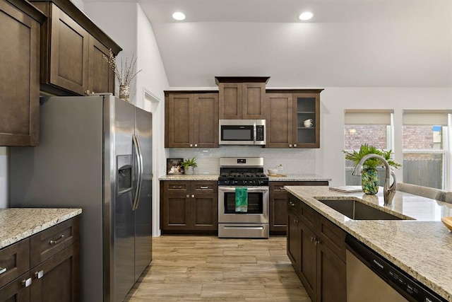 kitchen with a sink, tasteful backsplash, dark brown cabinets, light wood-style floors, and appliances with stainless steel finishes