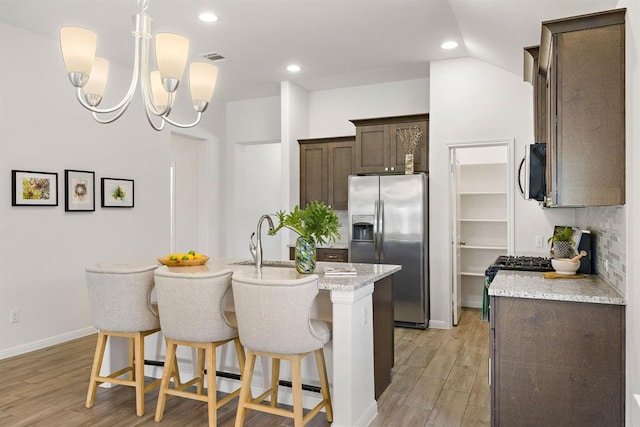 kitchen with a breakfast bar area, light wood-style flooring, appliances with stainless steel finishes, dark brown cabinetry, and a center island with sink