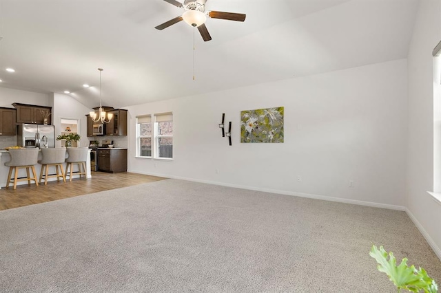 unfurnished living room featuring baseboards, recessed lighting, light colored carpet, lofted ceiling, and ceiling fan with notable chandelier