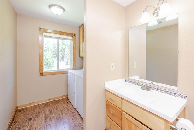 washroom featuring a sink, baseboards, light wood-style floors, separate washer and dryer, and cabinet space