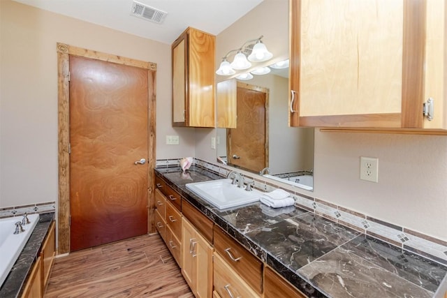 kitchen with dark stone countertops, visible vents, a sink, and light wood-style floors