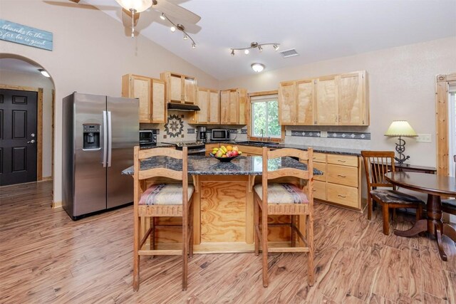 kitchen with lofted ceiling, light brown cabinetry, stainless steel appliances, arched walkways, and light wood-style floors