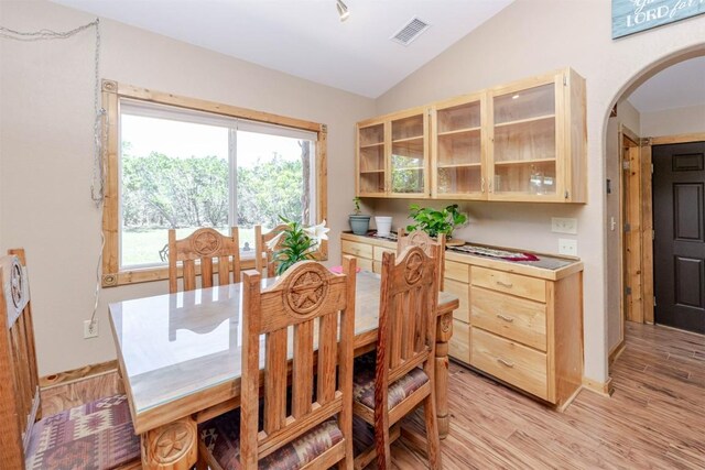 dining space featuring arched walkways, light wood finished floors, vaulted ceiling, and visible vents