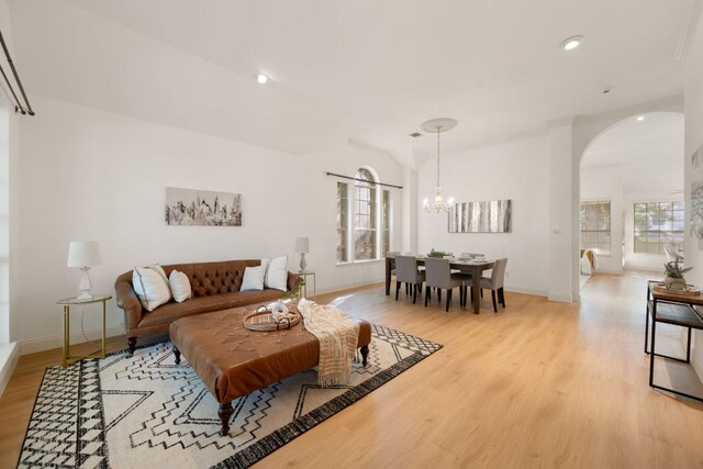 living room with plenty of natural light, light wood-style flooring, arched walkways, and an inviting chandelier