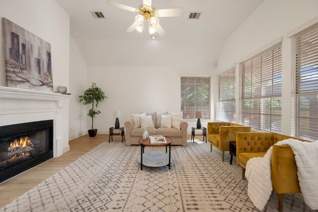 living room with ceiling fan, lofted ceiling, a lit fireplace, and visible vents