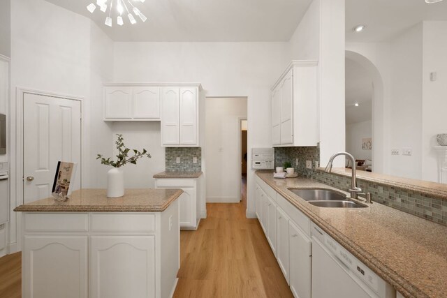 kitchen with white cabinets, arched walkways, a sink, tasteful backsplash, and dishwasher