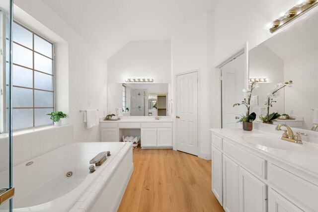 bathroom featuring two vanities, a sink, lofted ceiling, wood finished floors, and a whirlpool tub