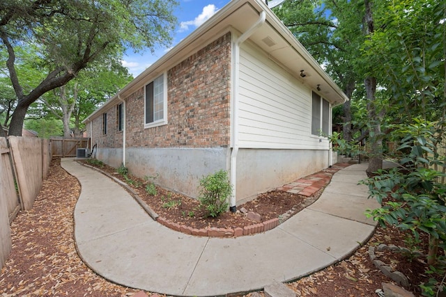view of property exterior featuring brick siding, central AC unit, and fence