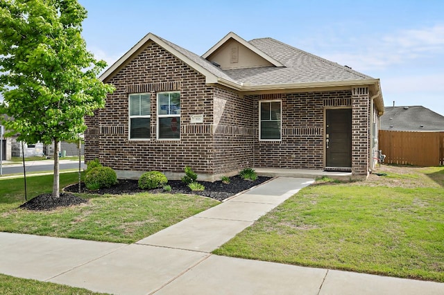 view of front of property featuring brick siding, a shingled roof, a front yard, and fence