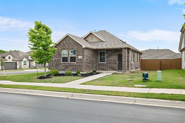 view of front facade featuring fence, brick siding, a front yard, and roof with shingles