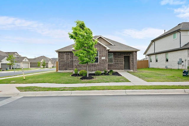 view of front of property featuring a front lawn, a shingled roof, fence, brick siding, and a residential view
