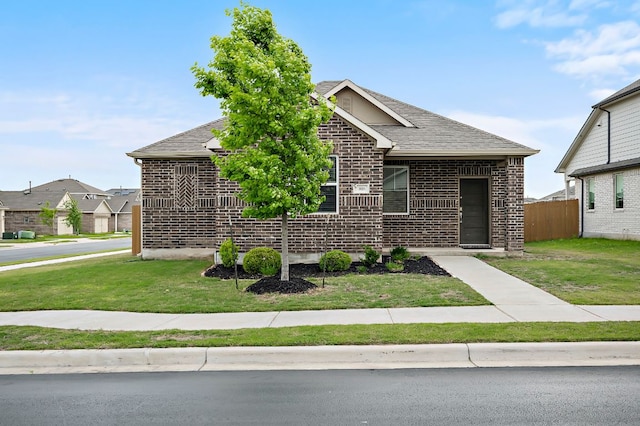 view of front facade featuring brick siding, fence, roof with shingles, and a front yard
