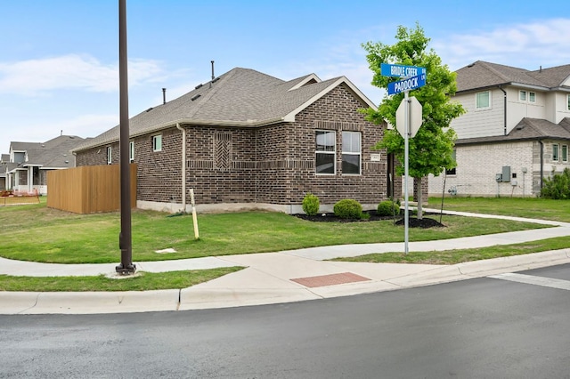 view of front of house featuring brick siding, a shingled roof, and a front yard