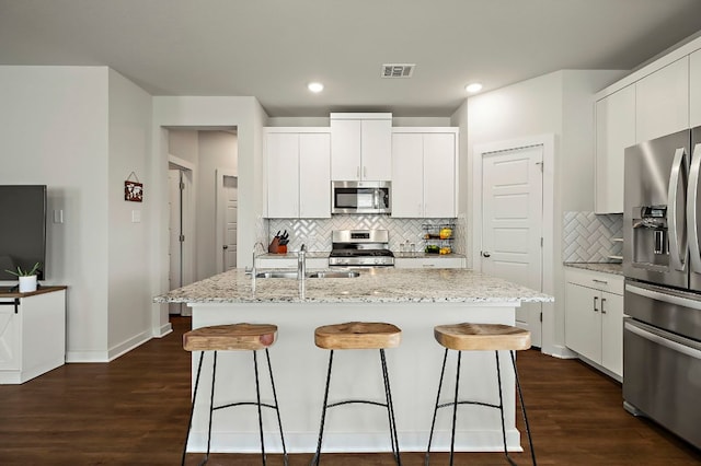 kitchen with a sink, a breakfast bar area, backsplash, appliances with stainless steel finishes, and visible vents
