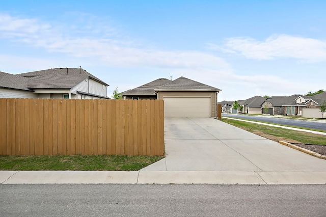 view of front of property with concrete driveway, fence, a residential view, and a garage