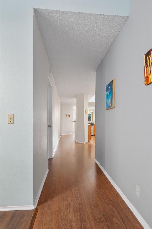 hallway with baseboards, wood finished floors, and a textured ceiling