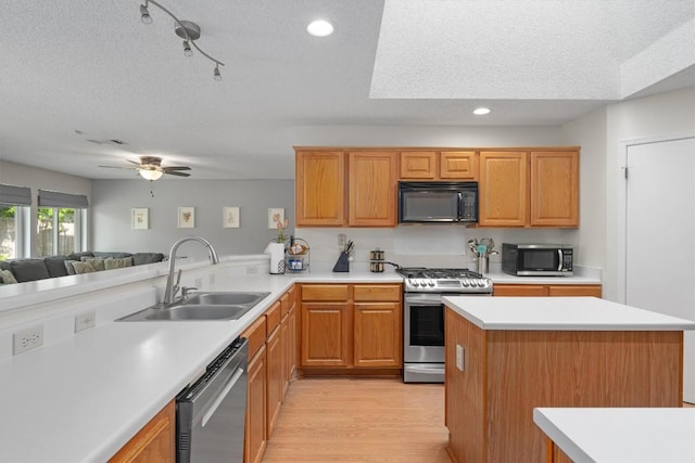 kitchen featuring light countertops, a sink, a textured ceiling, appliances with stainless steel finishes, and open floor plan
