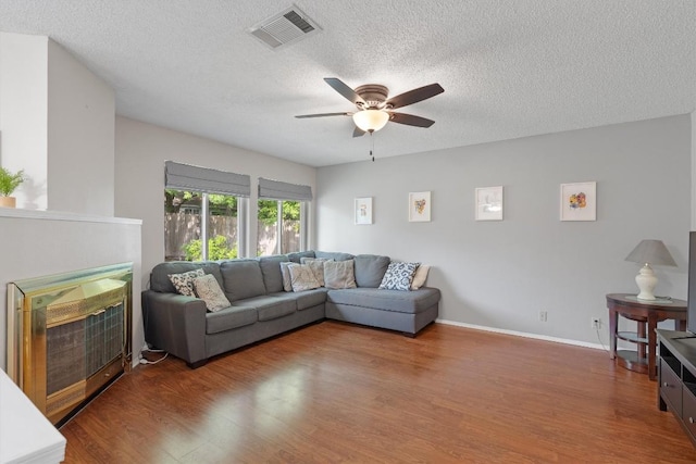living area featuring wood finished floors, a ceiling fan, visible vents, and a textured ceiling
