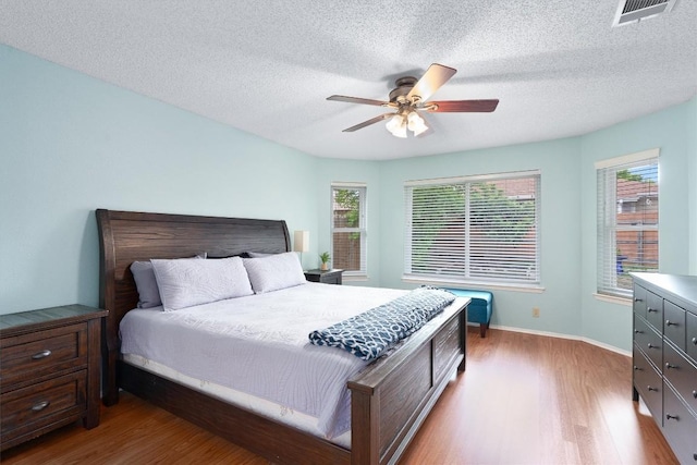 bedroom featuring wood finished floors, a textured ceiling, ceiling fan, baseboards, and visible vents