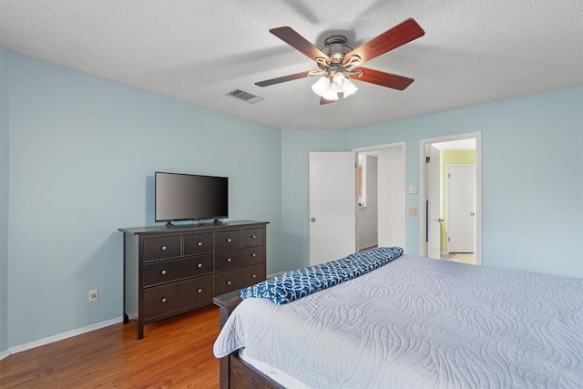 bedroom with wood finished floors, a textured ceiling, ceiling fan, baseboards, and visible vents