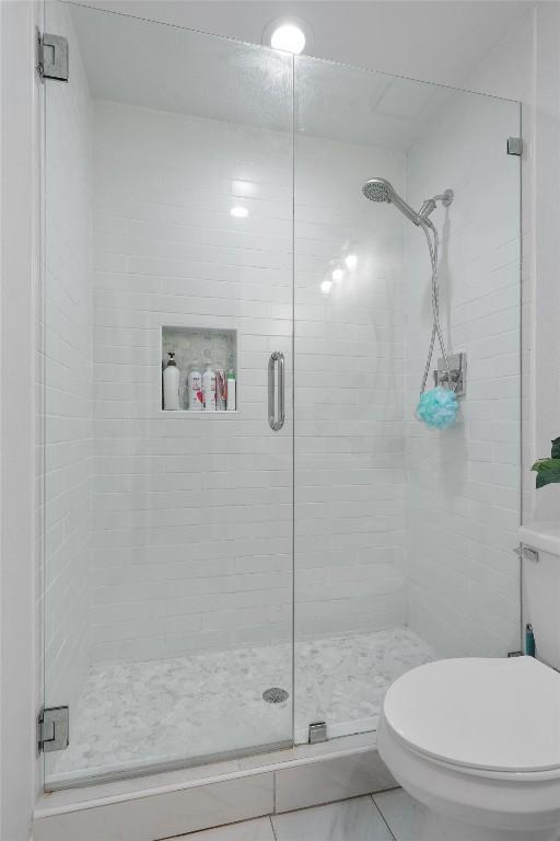 bathroom with a shower stall, toilet, and tile patterned floors