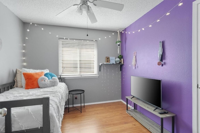 bedroom featuring wood finished floors, a textured ceiling, baseboards, and ceiling fan