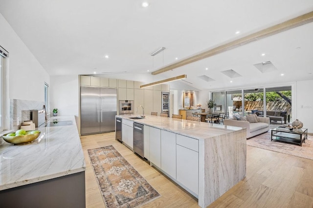 kitchen featuring light wood-style flooring, a sink, vaulted ceiling with beams, modern cabinets, and appliances with stainless steel finishes