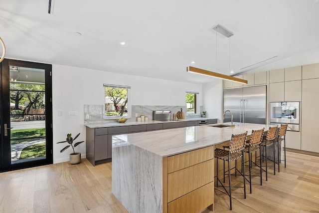 kitchen with a sink, light wood-style floors, modern cabinets, appliances with stainless steel finishes, and light stone countertops