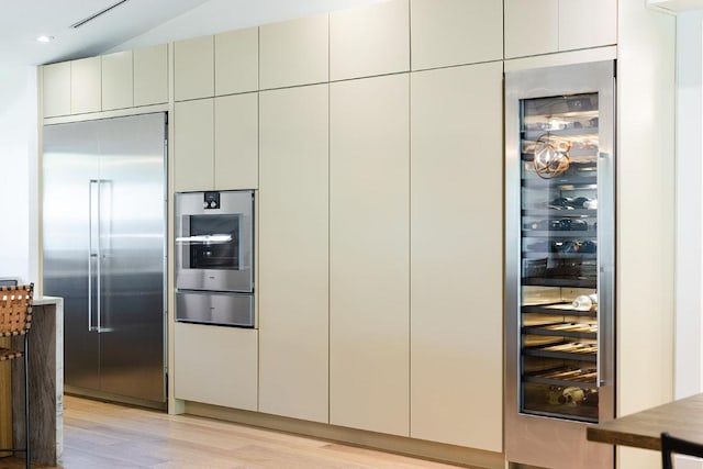 interior space with a warming drawer, stainless steel appliances, light wood finished floors, wine cooler, and recessed lighting