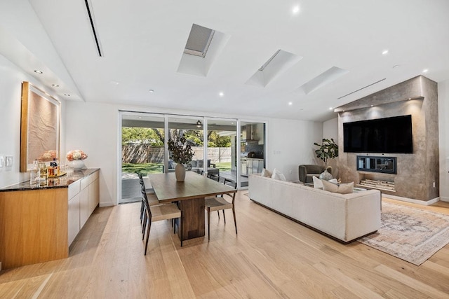 living area featuring light wood finished floors, baseboards, lofted ceiling with skylight, and recessed lighting