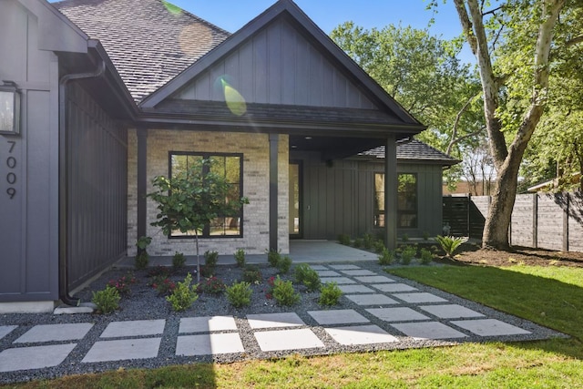view of front of home with a porch, board and batten siding, brick siding, fence, and a shingled roof