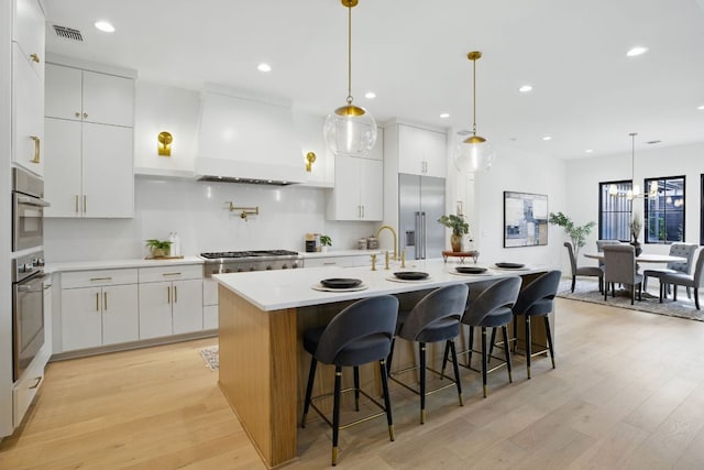 kitchen featuring a kitchen island with sink, light wood-style flooring, custom range hood, appliances with stainless steel finishes, and visible vents