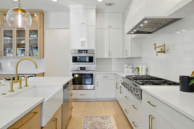 kitchen with a sink, appliances with stainless steel finishes, visible vents, light wood-style floors, and wall chimney exhaust hood