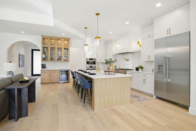 kitchen featuring recessed lighting, wine cooler, custom range hood, light wood-style flooring, and appliances with stainless steel finishes