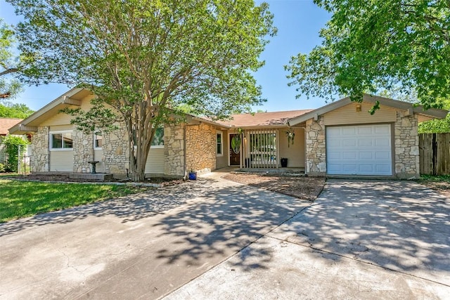 ranch-style home featuring concrete driveway, an attached garage, fence, and stone siding