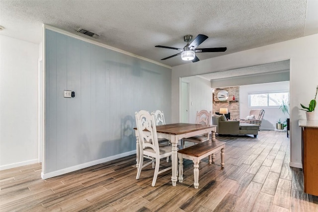 dining room featuring light wood finished floors, a textured ceiling, baseboards, visible vents, and ceiling fan
