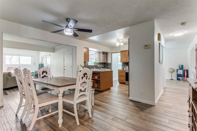dining room featuring a ceiling fan, baseboards, a textured ceiling, and light wood-style flooring