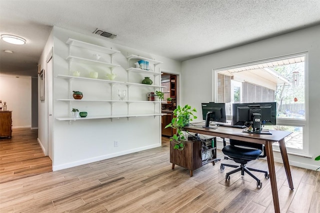 office featuring baseboards, a textured ceiling, visible vents, and light wood-type flooring