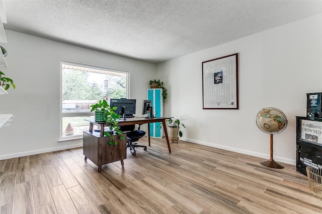 office space with baseboards, light wood-style floors, and a textured ceiling